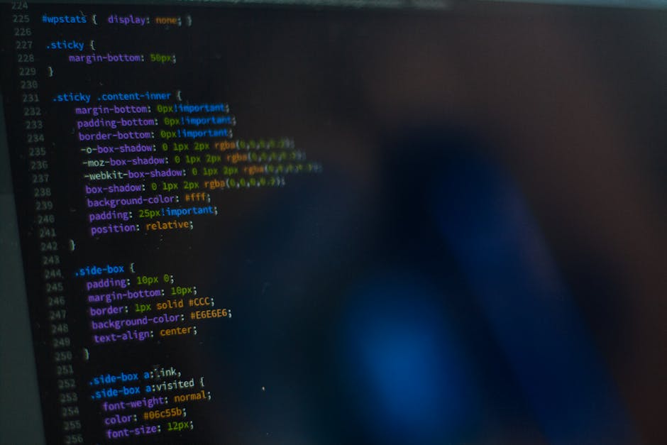 Close-up image of a computer screen displaying layered lines of colorful HTML or CSS code on a dark background. The code includes various styling elements such as margins, padding, borders, box shadow
